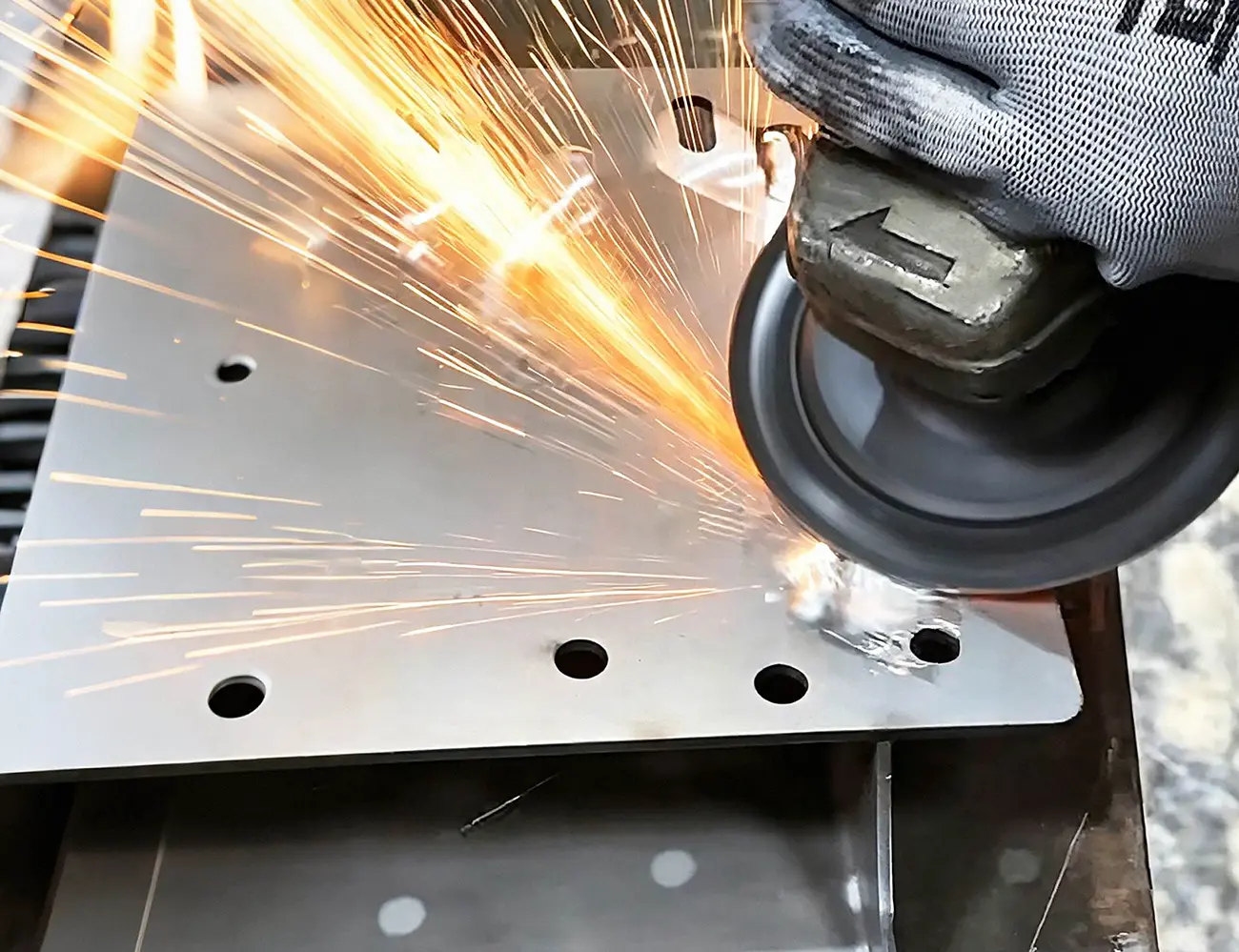 Factory worker grinding stainless steel plate with angle grinder, surface finishing process for custom sheet metal components